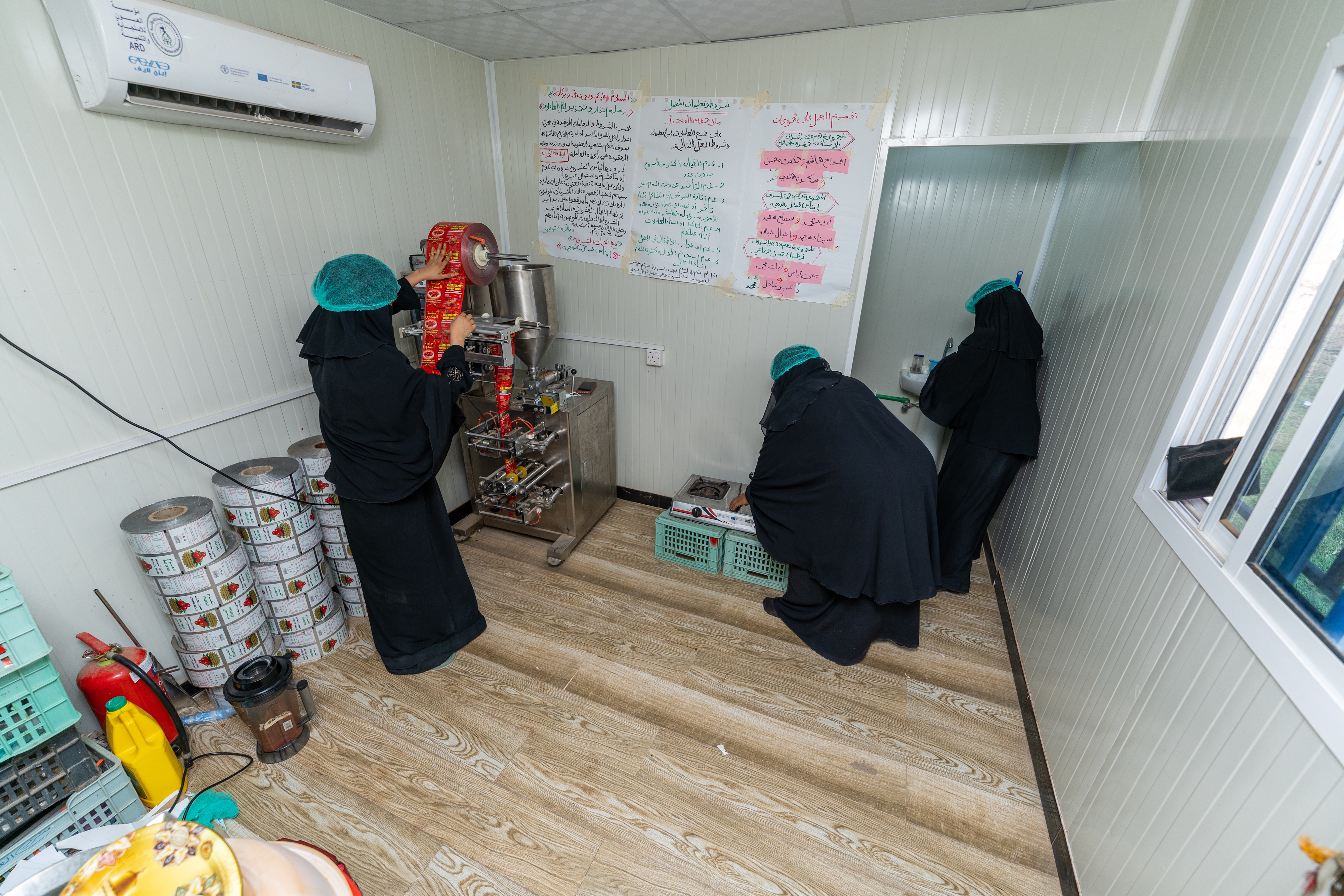 Mona, Iqbal, and Abeer working together in their food processing unit.