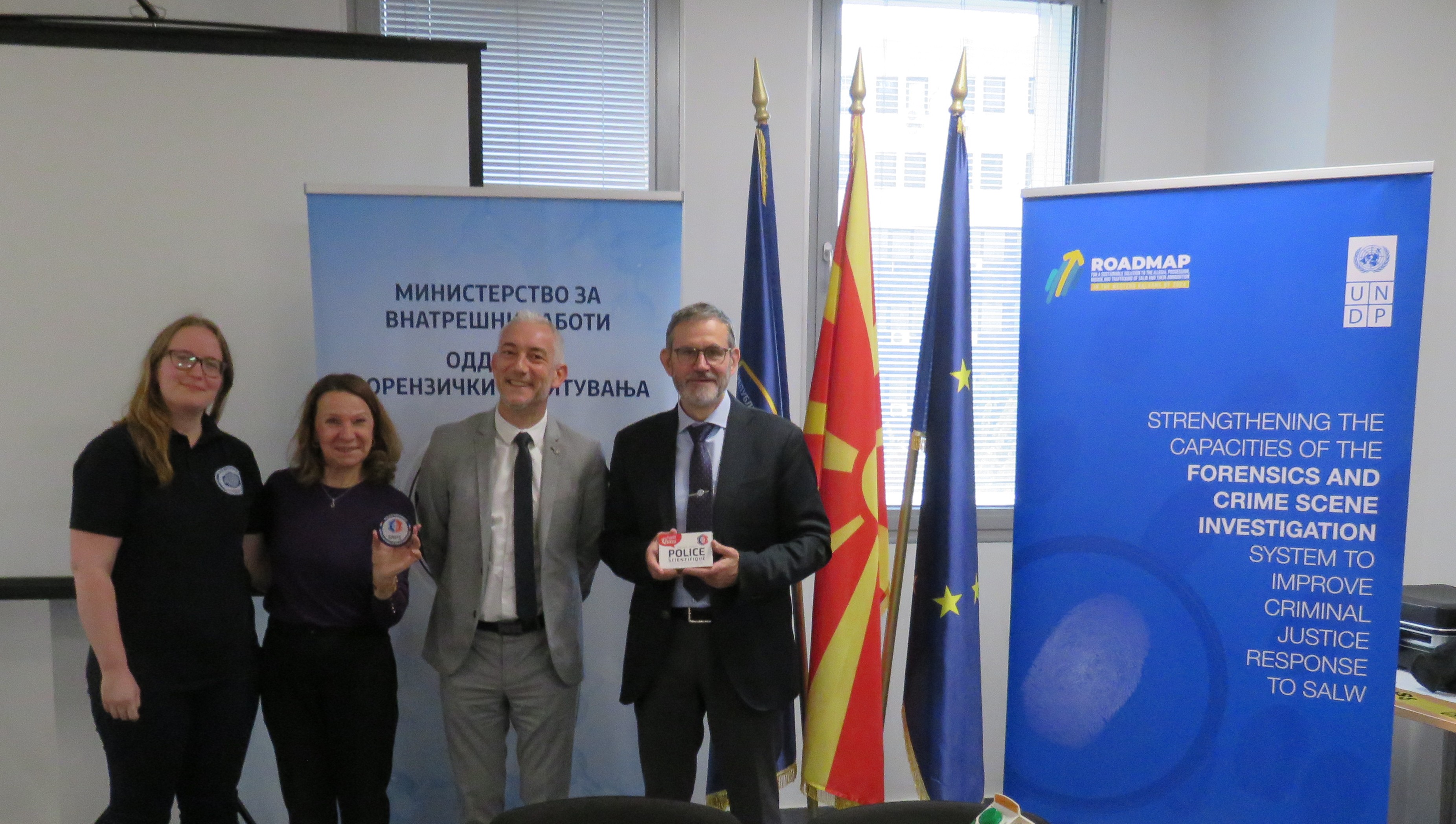 N Balkans SALW 4 members of the North Macedonia Ministry of Interior, the French National Forensic Police Department, and UNDP posing for a photo in front of country flags and program banners