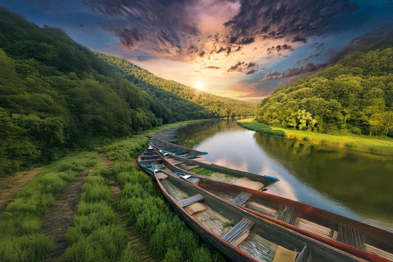 Image for the Practitioner’s corner of the MPTFO newsletter December 2024: idyllic nature scene, boats on the side of a river bend, lush green path with tire tracks, a sunset on a semi-moody sky