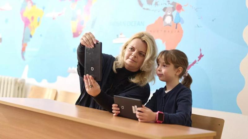 A teacher and student in a class room holding tablets; a world map in the background